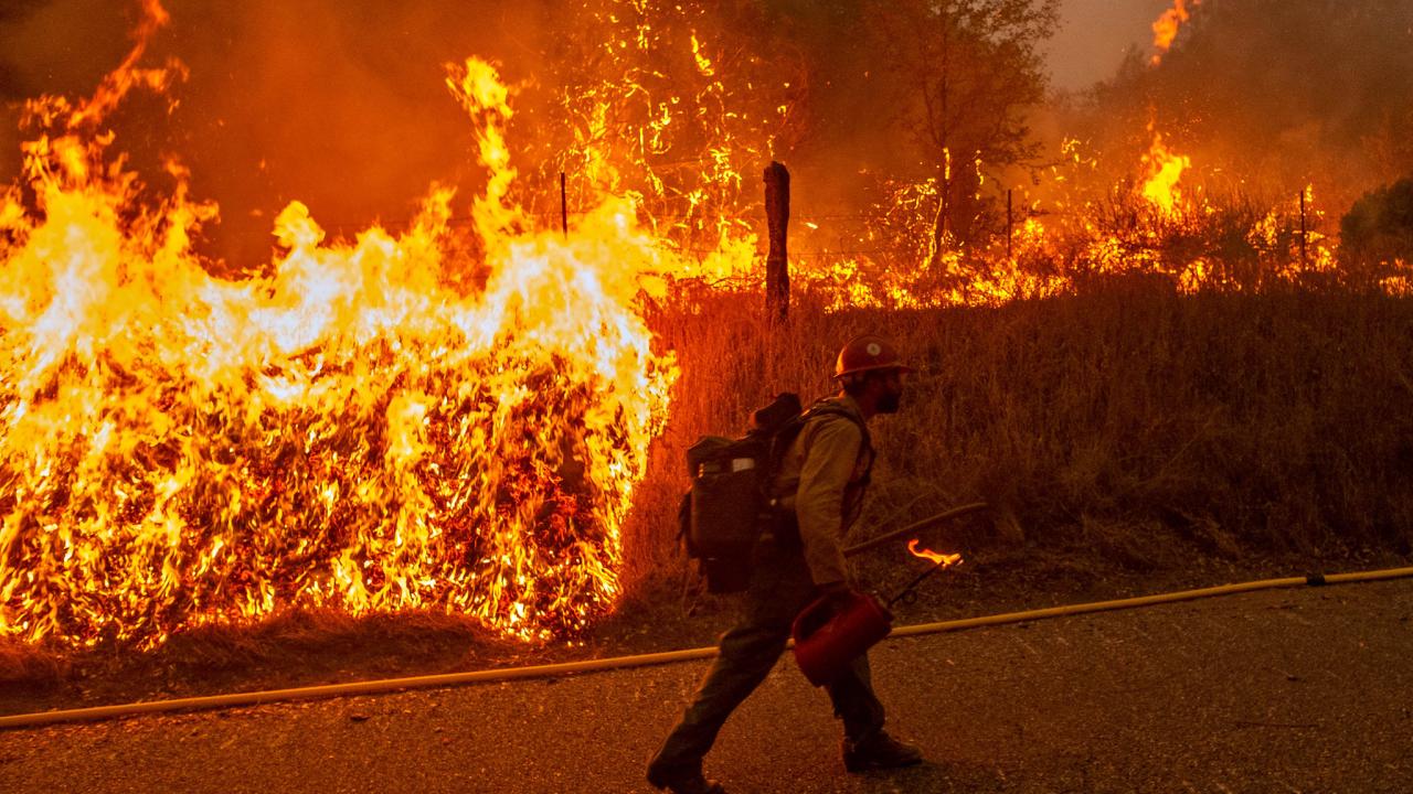 Firefighter walks along highway with flames to his side during Creek Fire response in 2022.