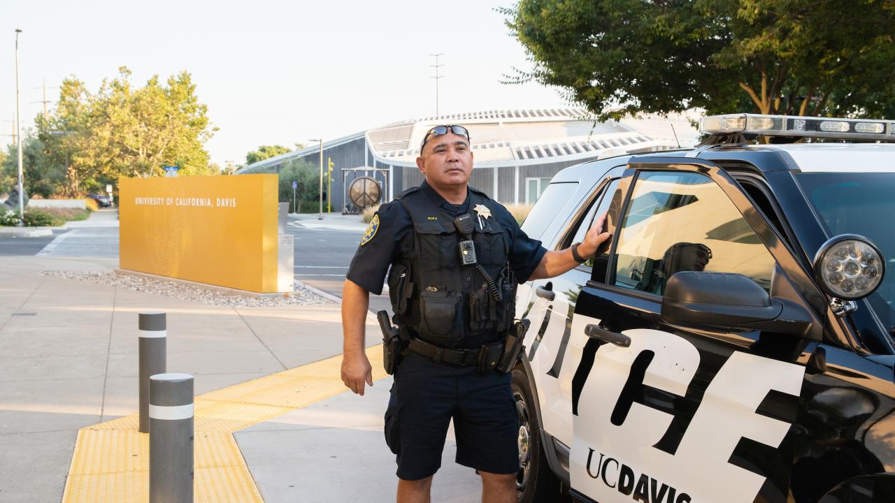 Campus police officer standing beside UC Davis patrol car on sunny sidewalk