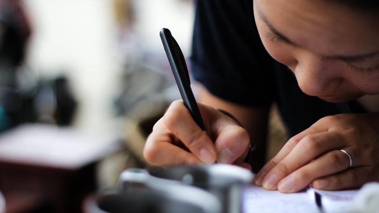 female bent over journal with pen writing