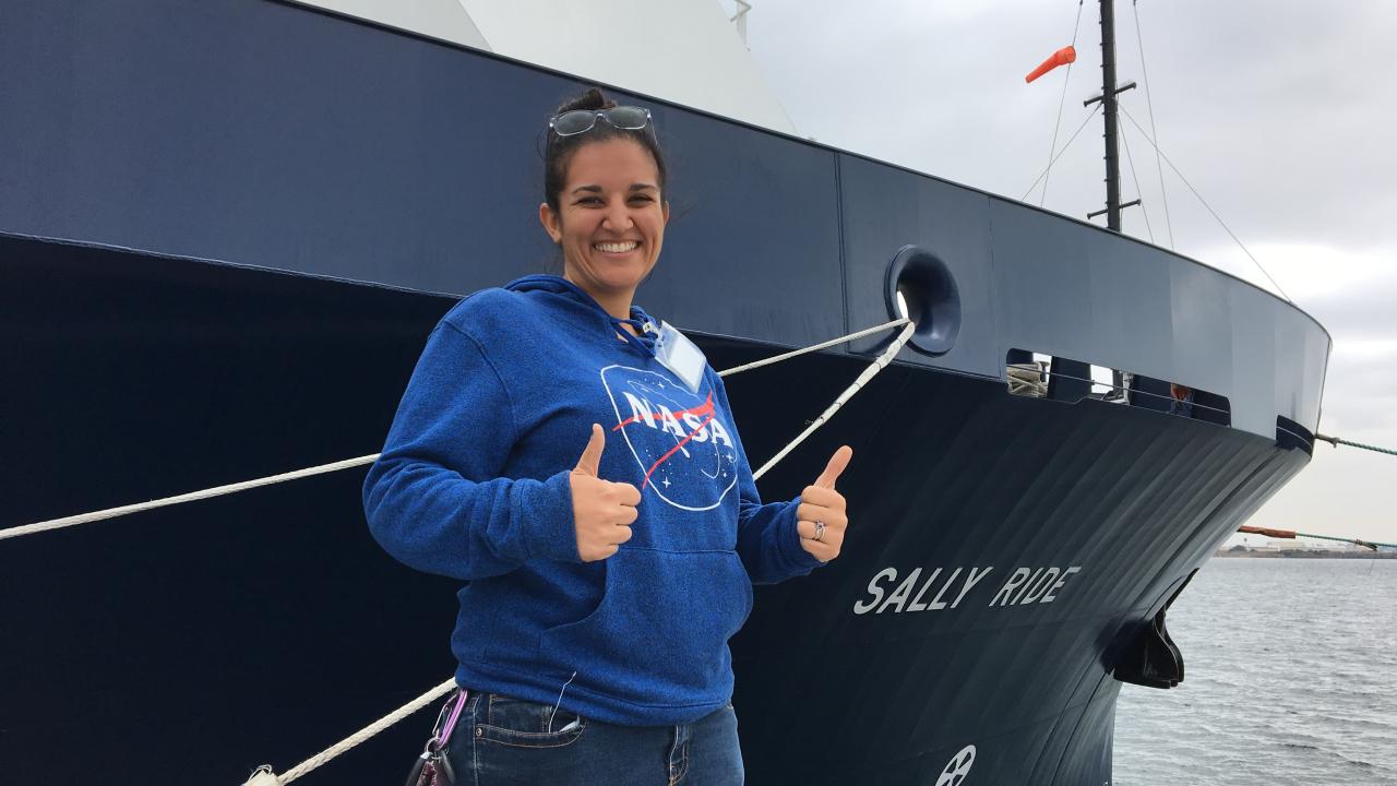 Woman in NASA sweatshirt stands in front of boat called Sally Ride