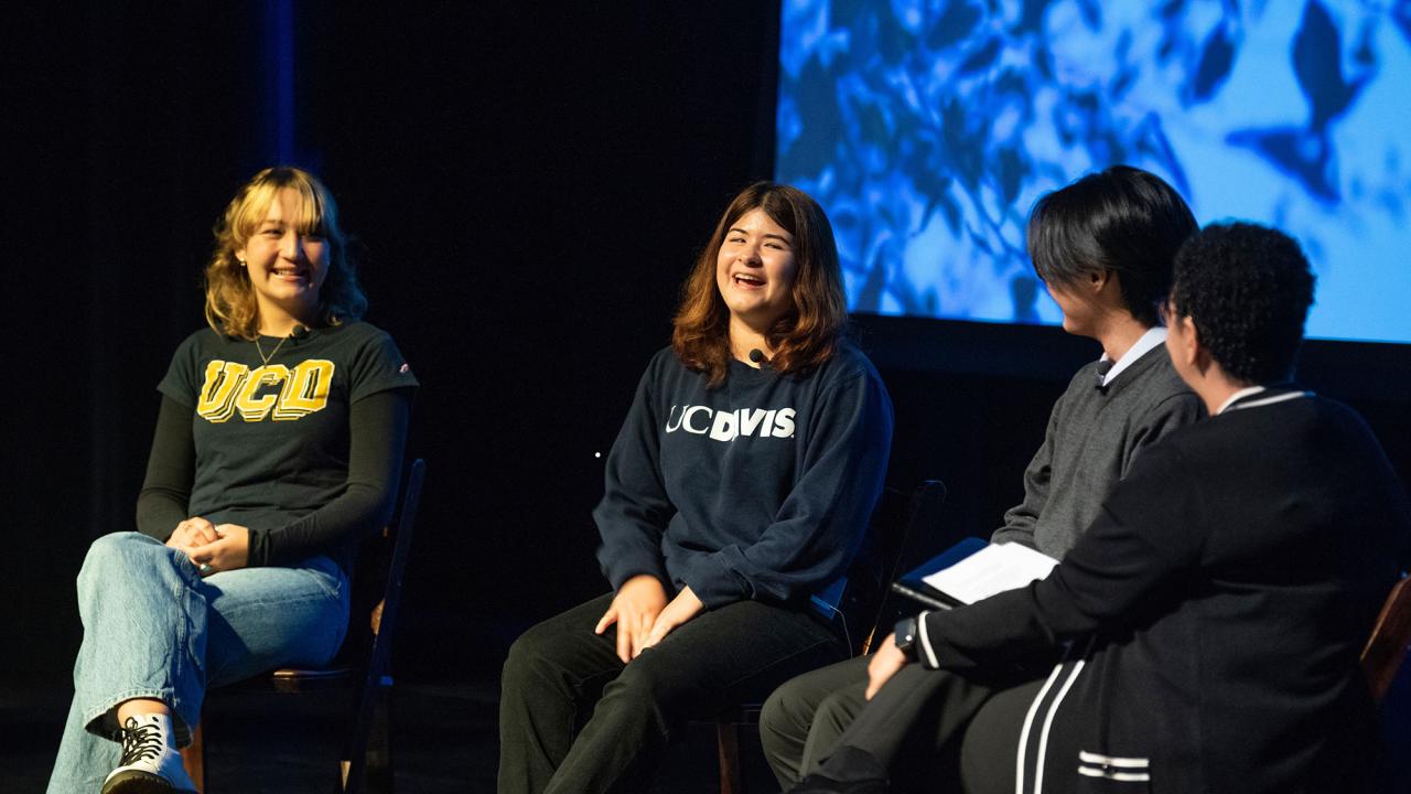 Three students and a woman seated with a screen behind them