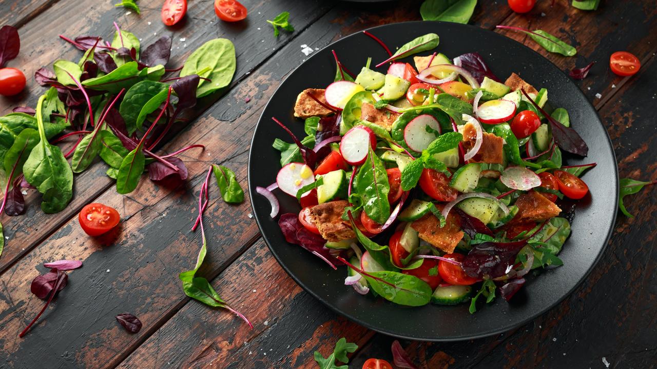 Mixed salad in dark bowl—greens, cherry tomatoes, radish slices and avocado on rustic wood