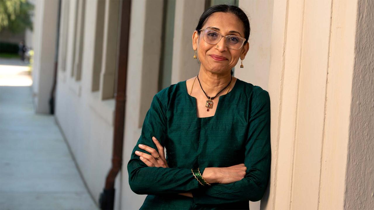 Smiling woman in a green outfit stands with arms crossed against a wall.