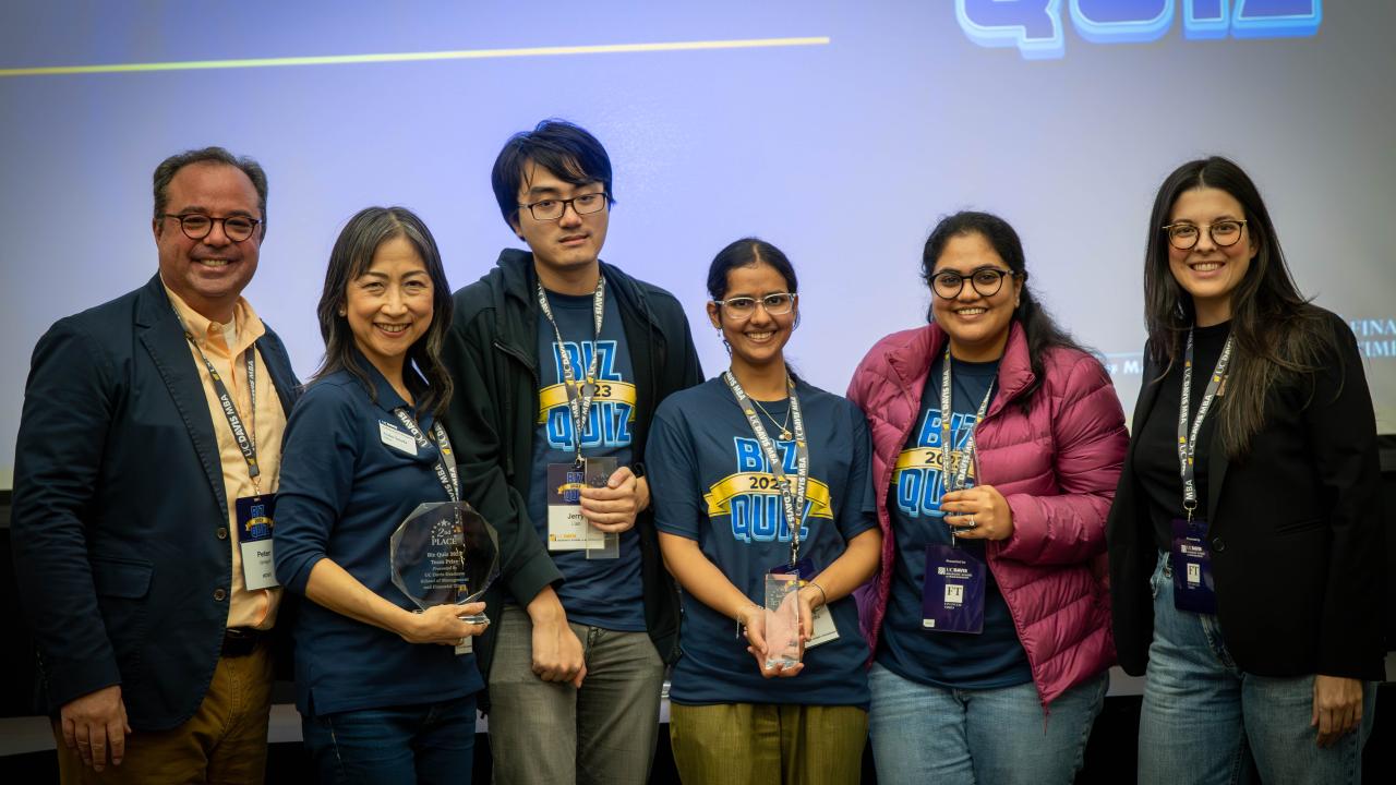 Students from previous Biz Quiz pose with awards in front of Biz Quiz backdrop