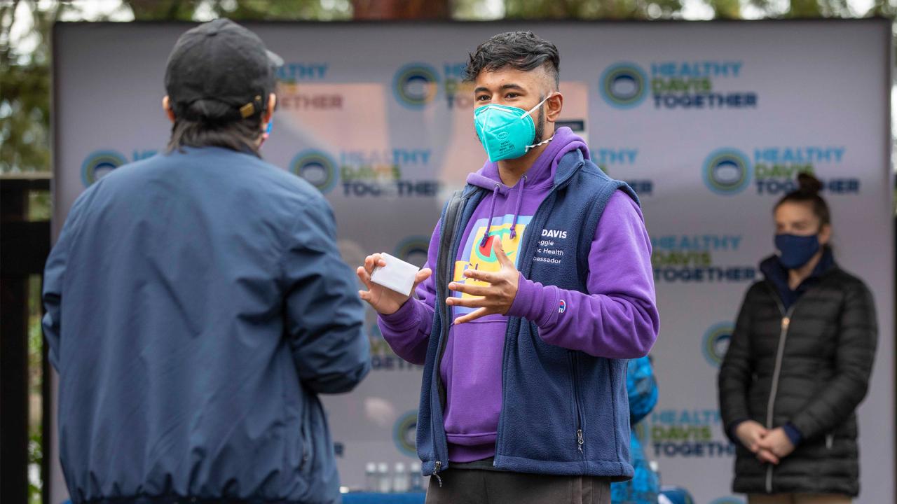 An individual holding a gift card gestures while talking with a second persono a sec