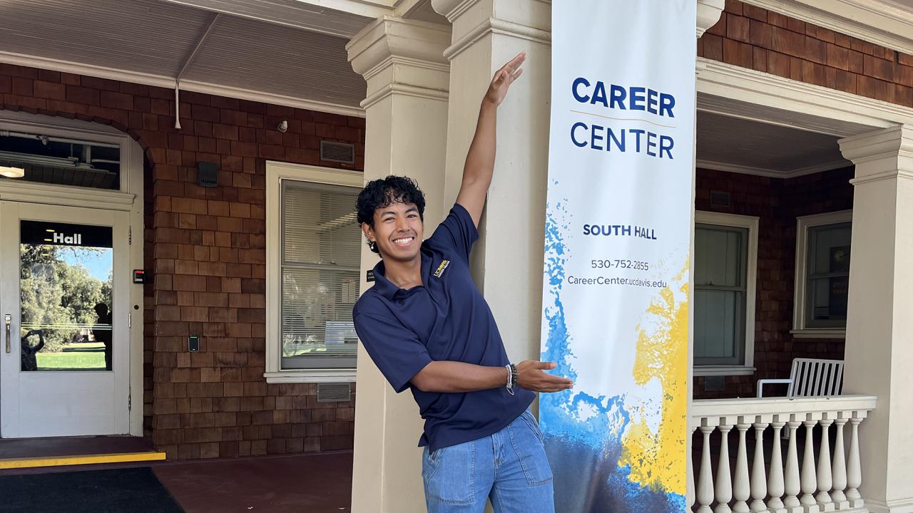 Nick Conti stretches upward to show off a tall banner with the Career Center name.