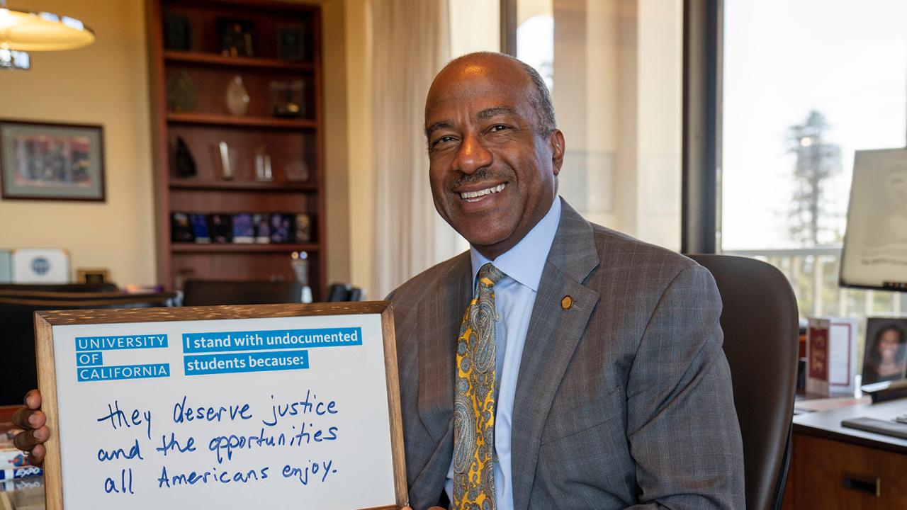 Photo of chancellor Gary S. May holding a white board that says "I stand with undocumented students because: They deserve justice and the opportunities all Americans enjoy."