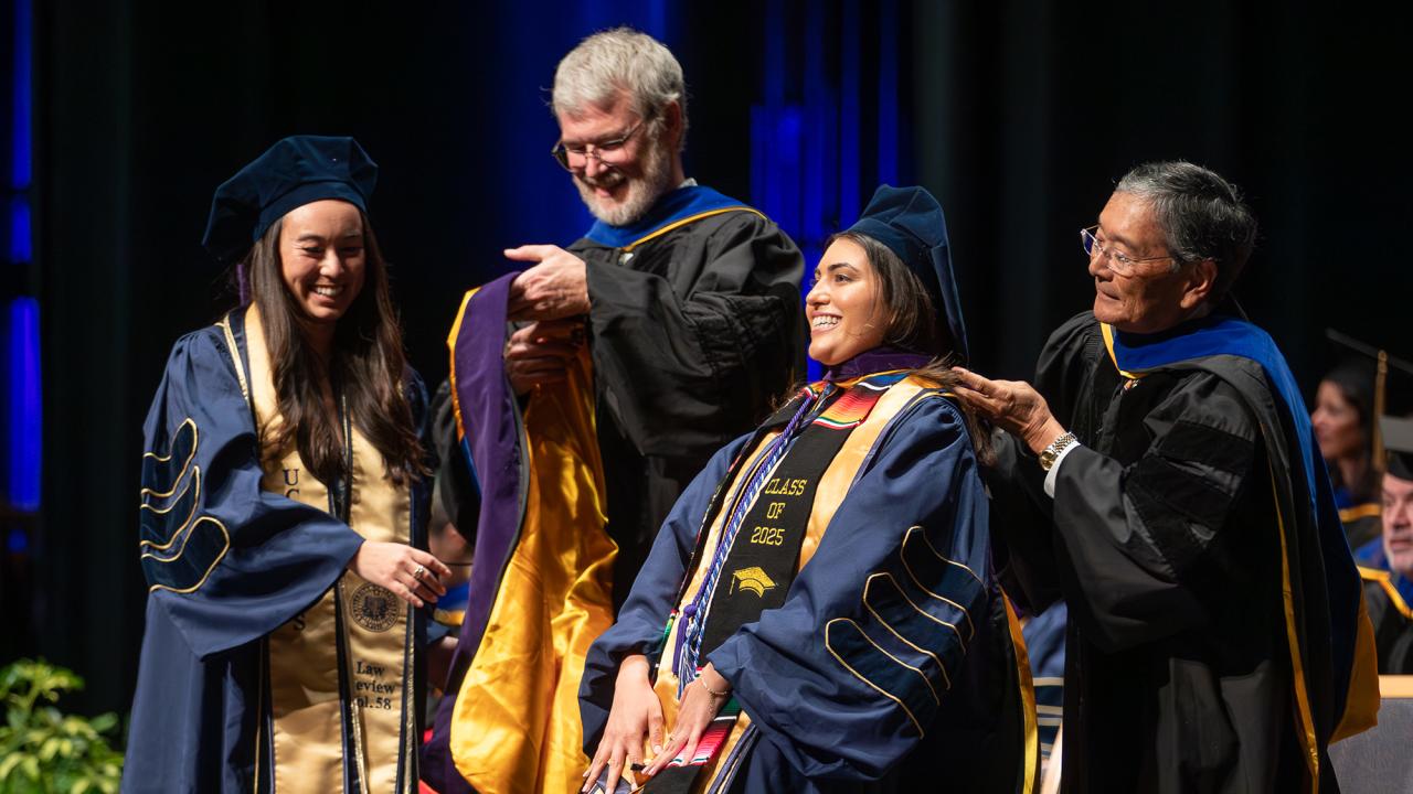 Two faculty in robes hooding smiling graduates at commencement