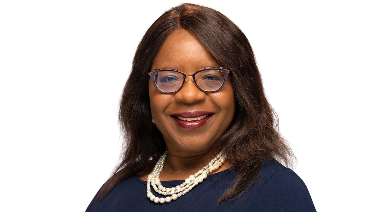 Smiling woman with glasses and pearl necklace, studio headshot on white background