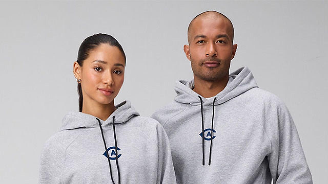 Two adults side-by-side wearing matching light-gray hoodies with a small blue logo