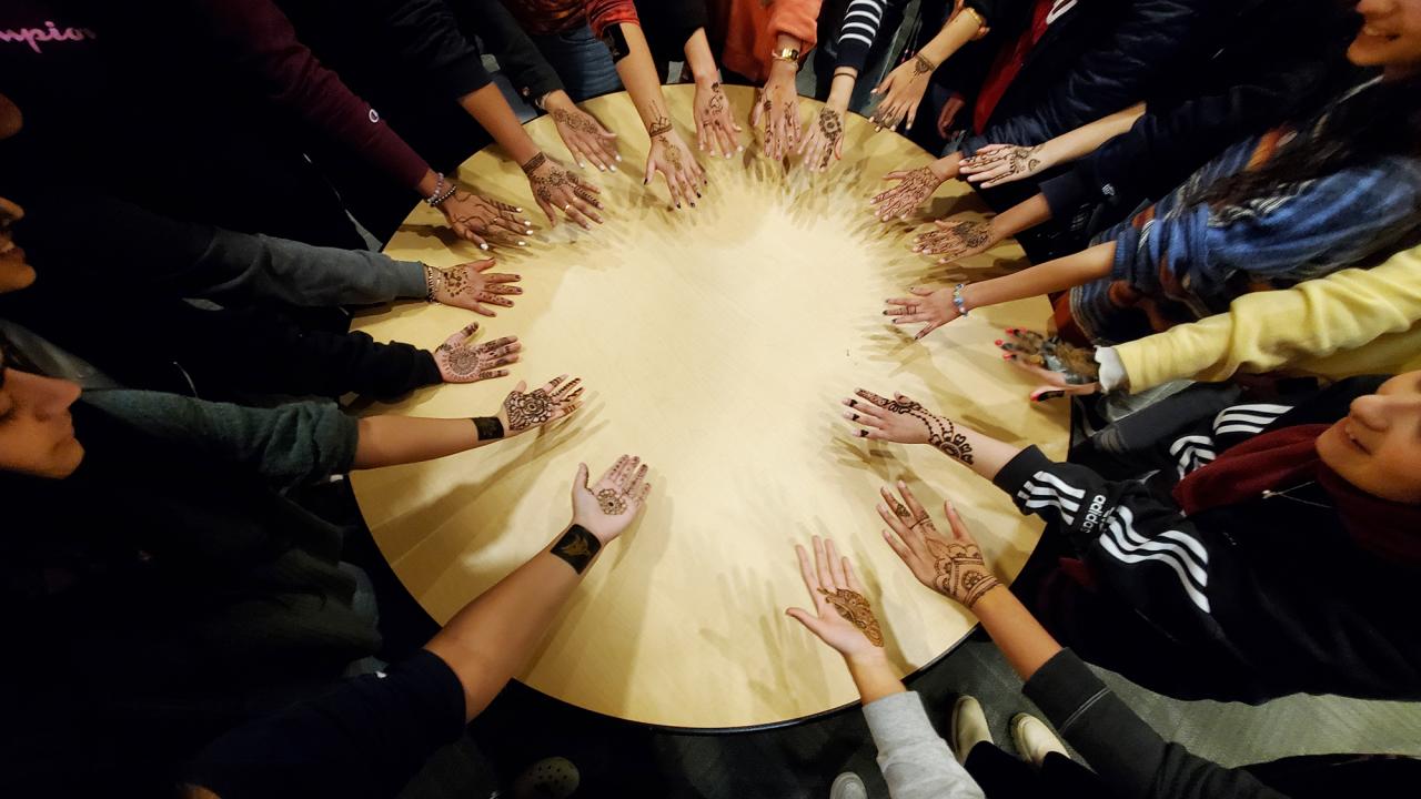 Students put their hands in a circle to show off their henna designs. 