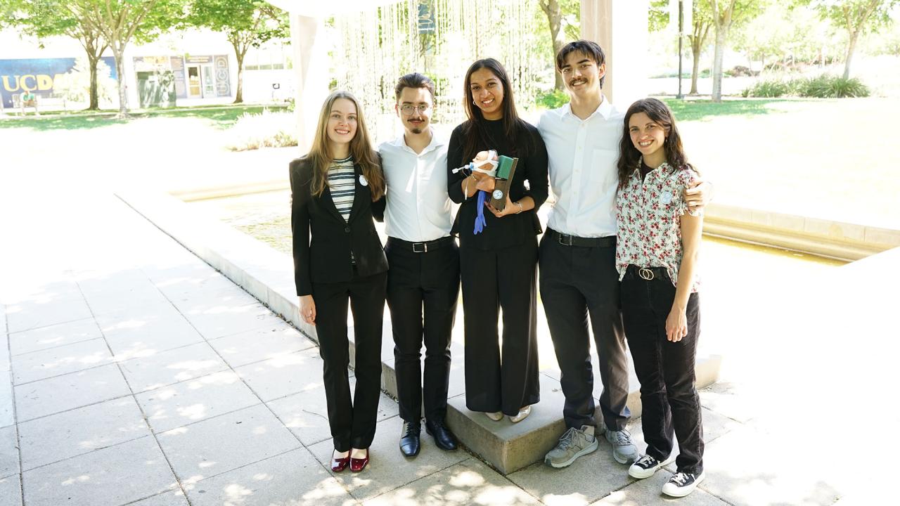 Six students in casual clothing standing by a courtyard fountain, smiling