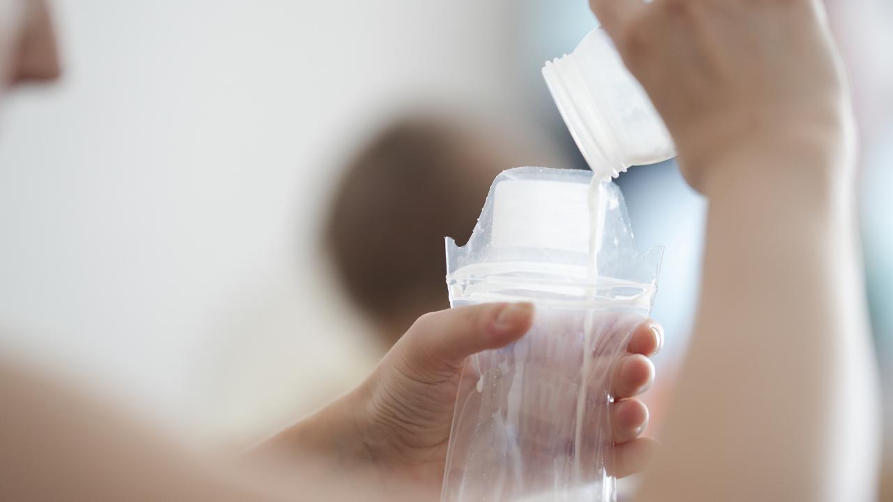 Hand pouring formula into bottle with blurred background. 