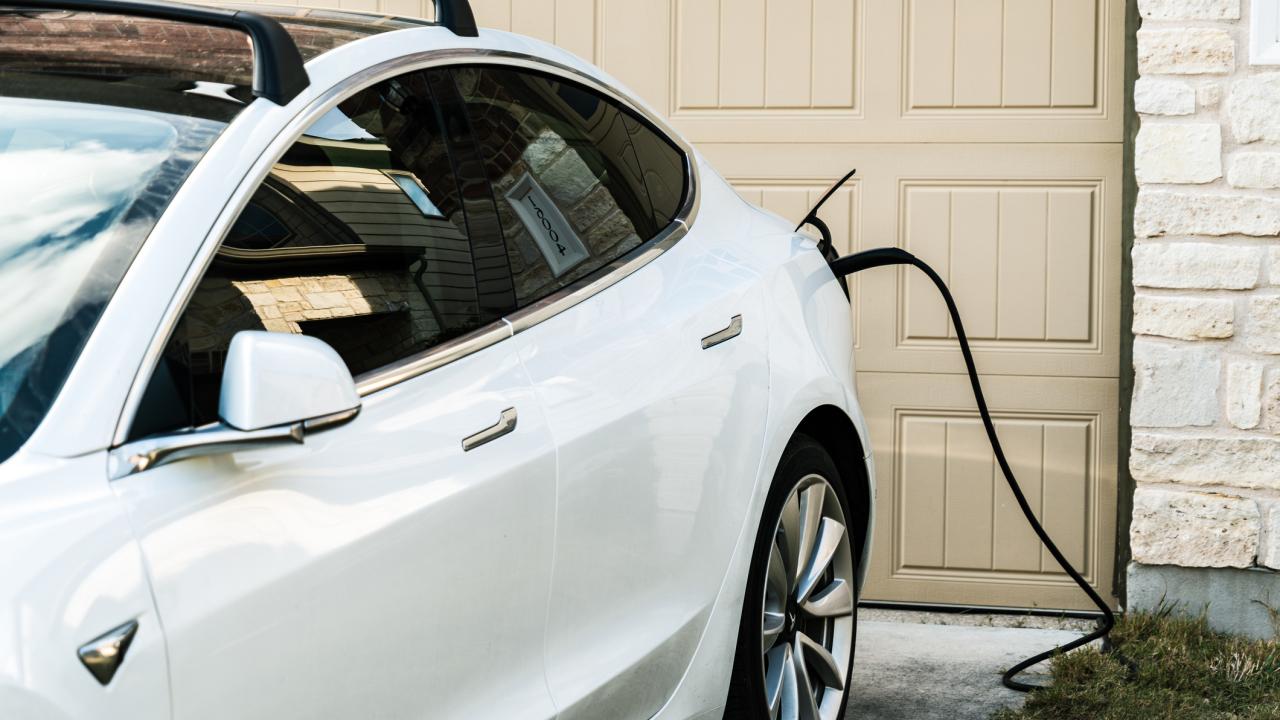 White electric SUV plugged into a home garage charger beside beige garage door