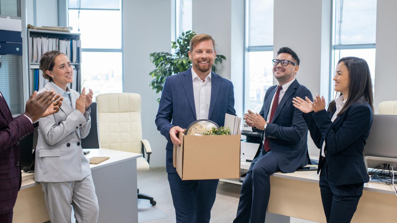 Workers convene in office, one with box