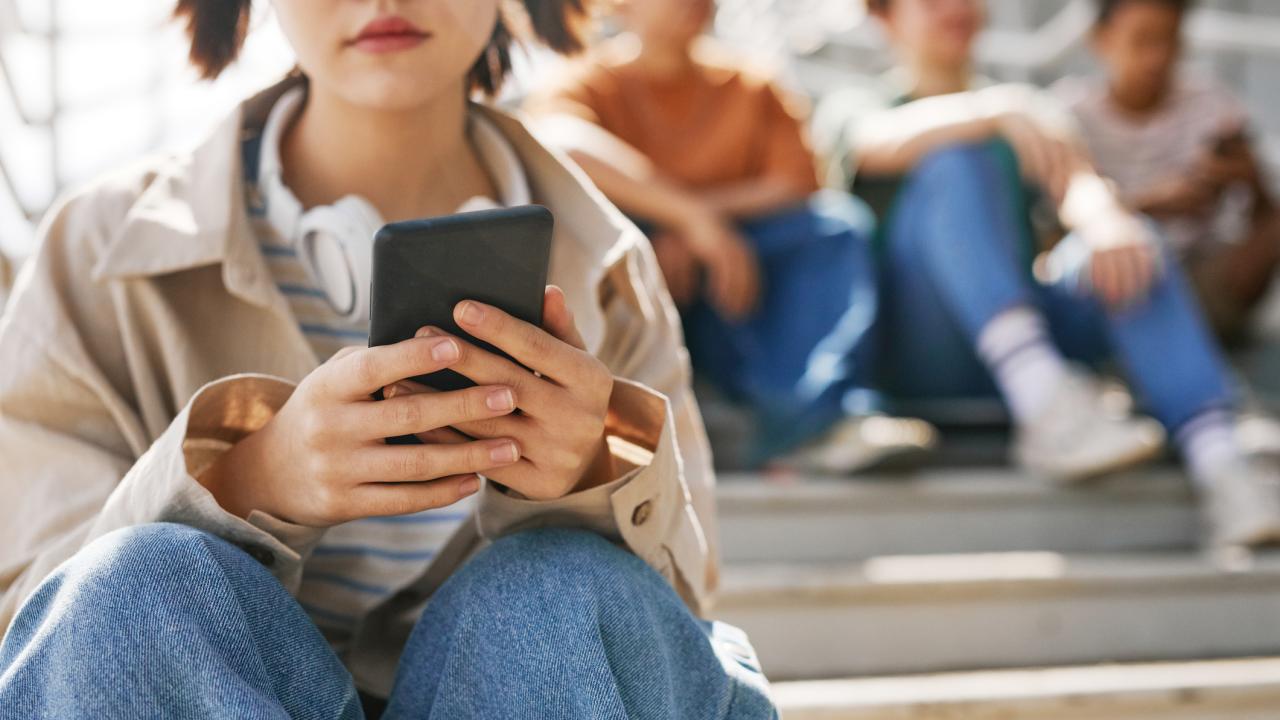 Young girl on cell phone sitting on steps with other youth behind her