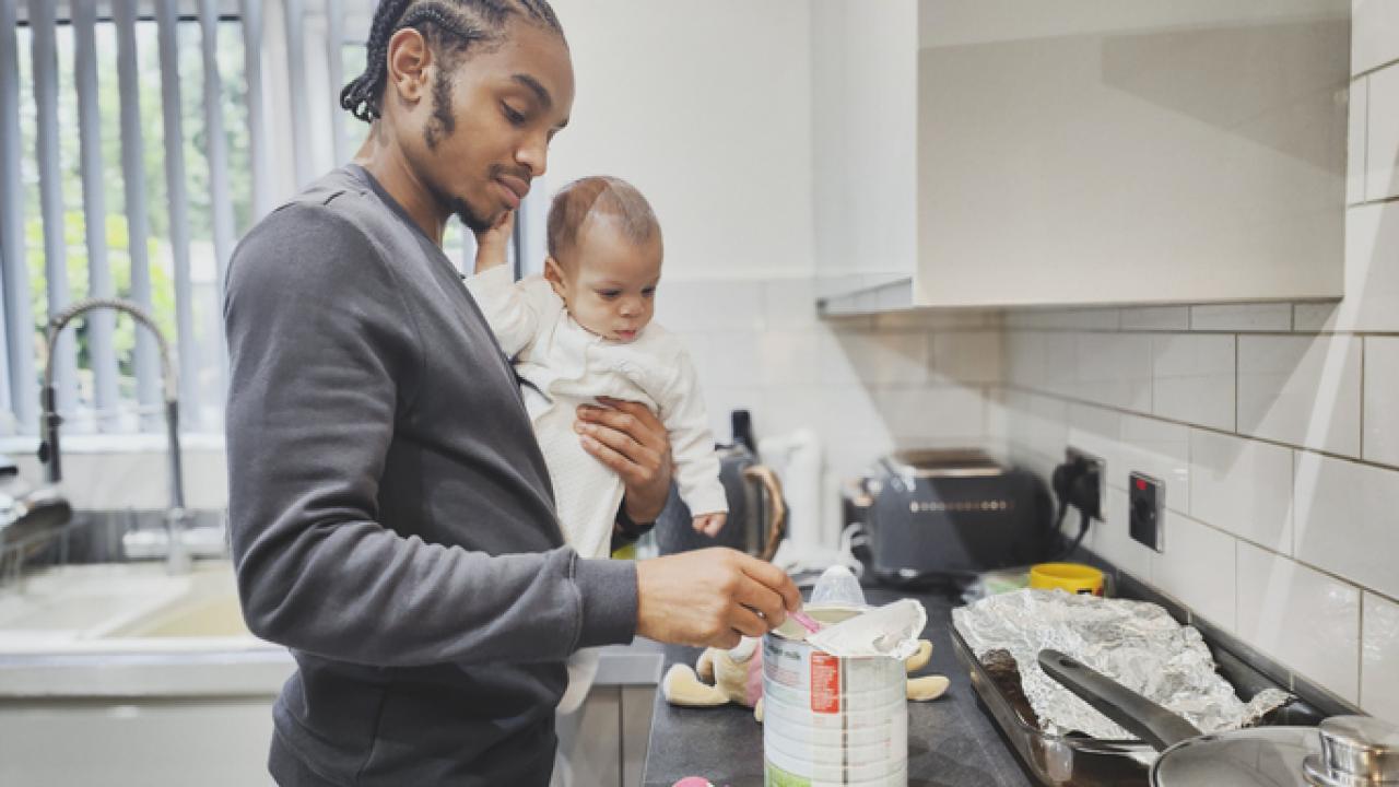 Man holding baby in his arms as he prepares infant formula. A new survey shows 81 percent of parents were forced to switch infant formulas during the May 2022 shortage, leading to undesirable health effects for babies.