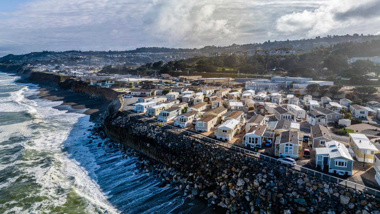 Aerial photo of coastal homes on rocky shoreline with crashing waves and cloudy sky