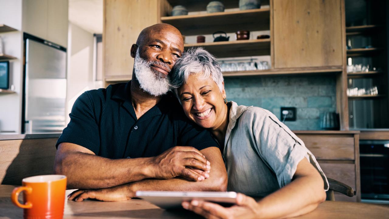 Two dark complected people sitting next to coffee cup in kitchen
