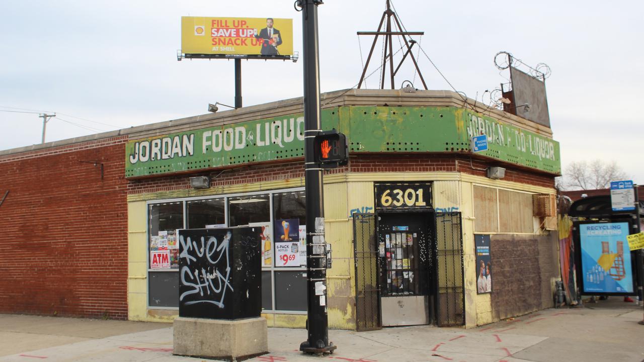 Corner store with a green awning, brick exterior, and a street sign nearby.