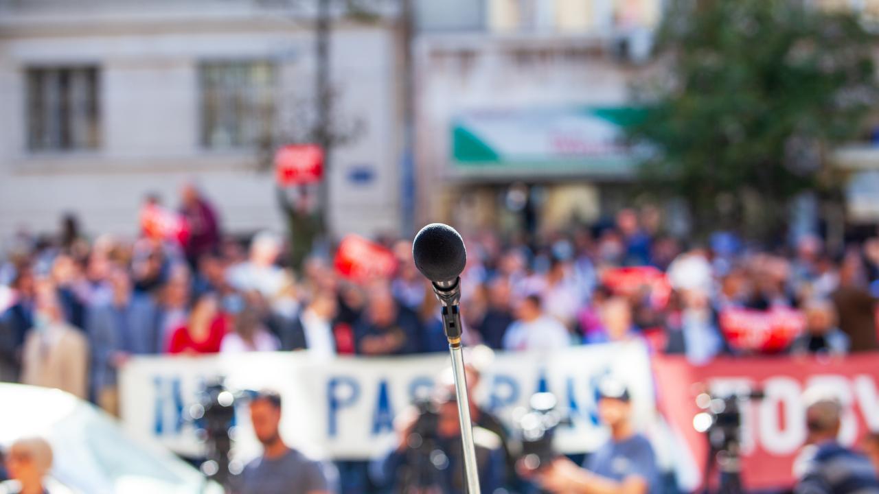 Microphone on stand at outdoor rally, blurred crowd and banners in background