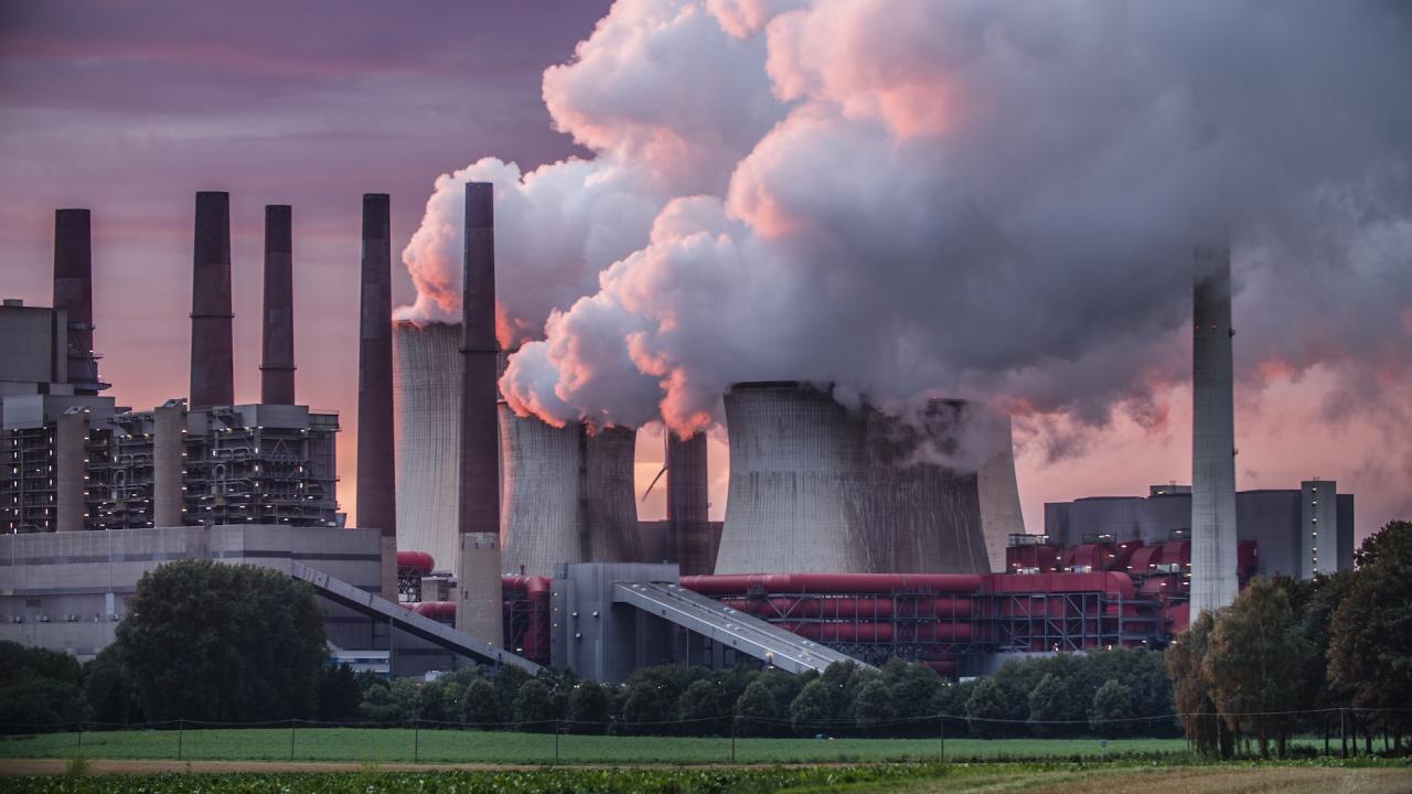 Power station chimneys emit billowy clouds of smoke and steam aainsta dramatic red sunset light. 