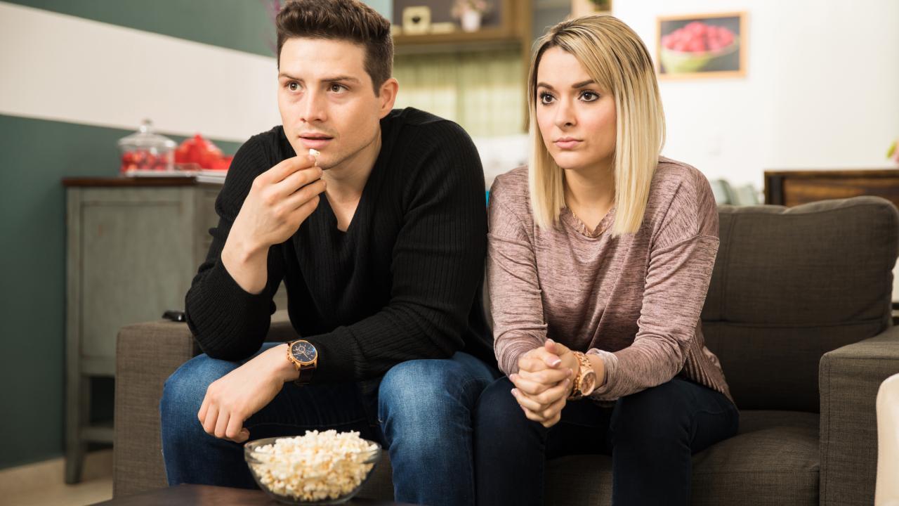 Man and woman watching television of movie in home looking intently