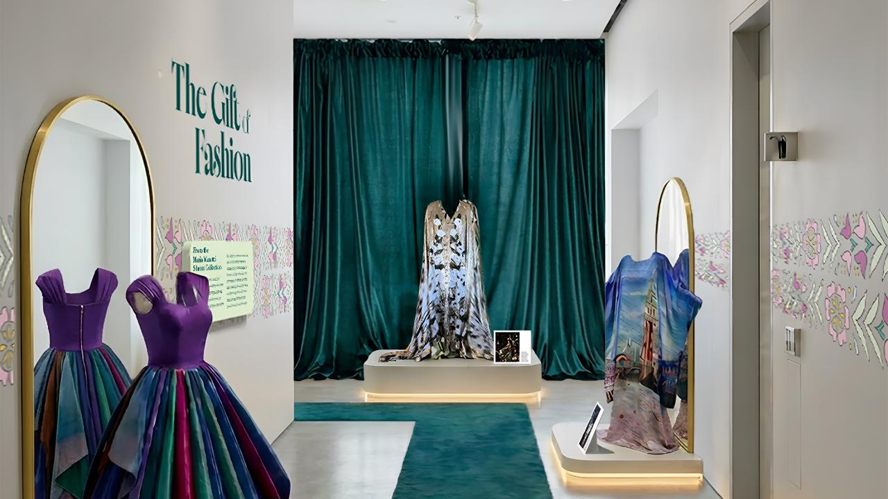 Gallery with mannequins in iridescent gowns, large mirrors, teal runner, and emerald curtains.