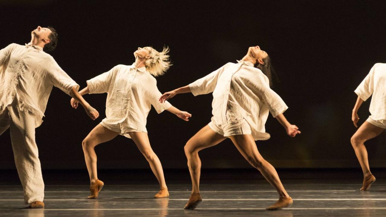 Dancers in white against black stage backdrop