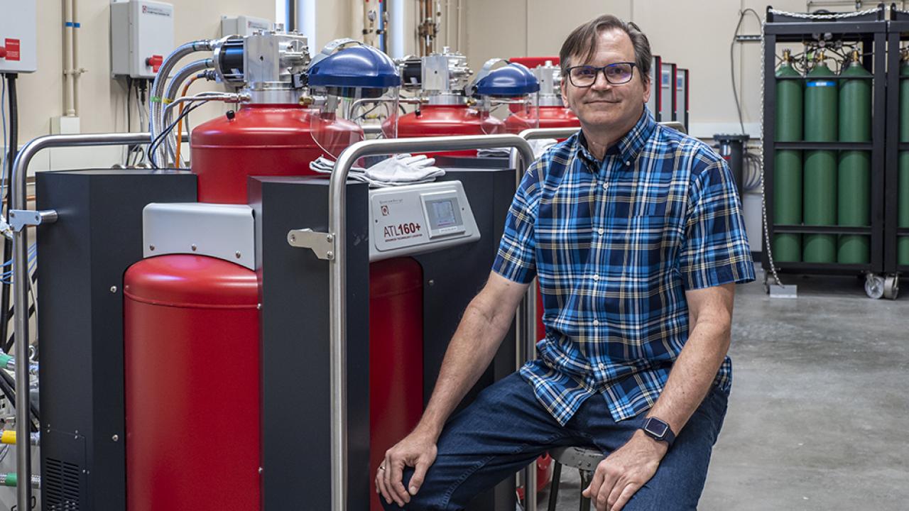 Seated male scientist next to helium recovery equipment 