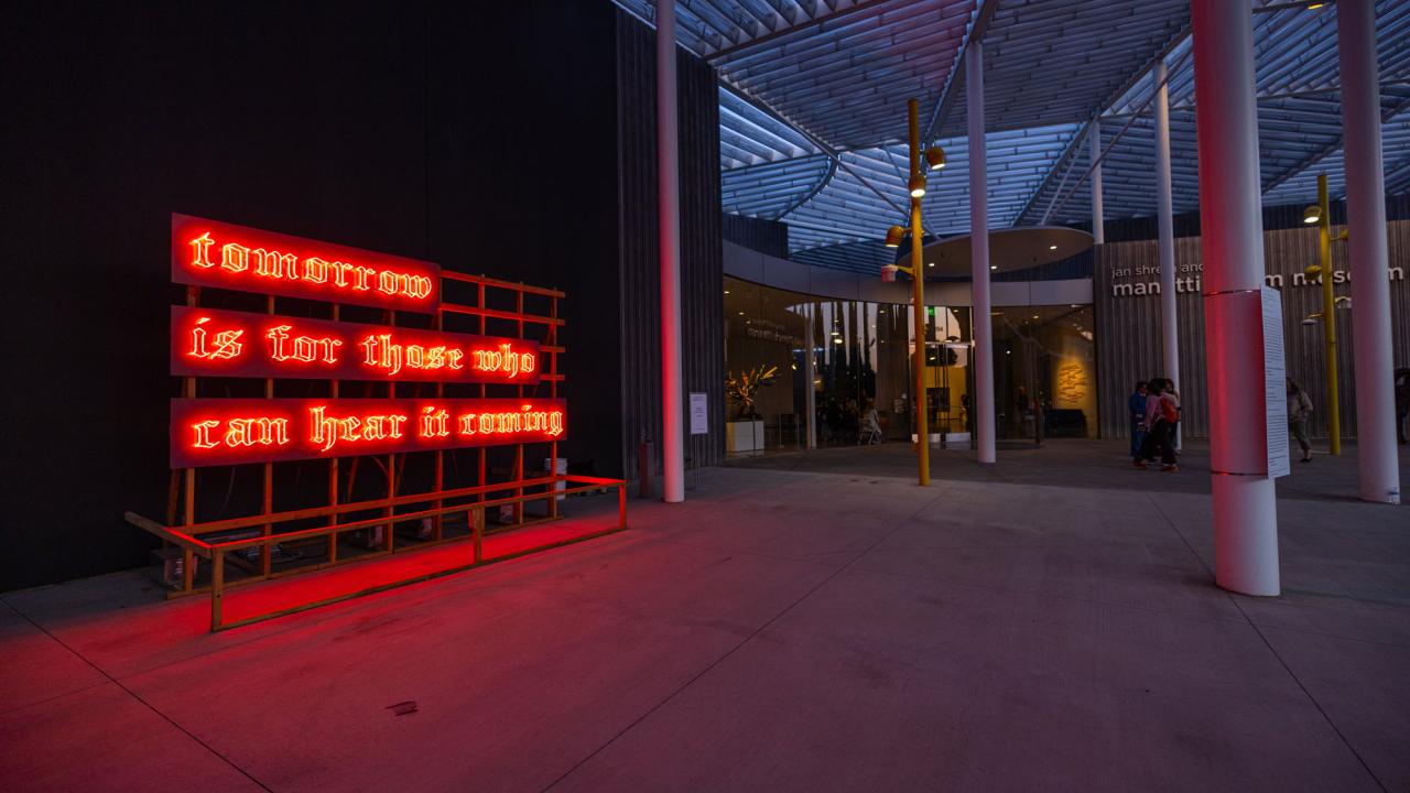 Neon sign, in orange, photographed at dusk in front of museum