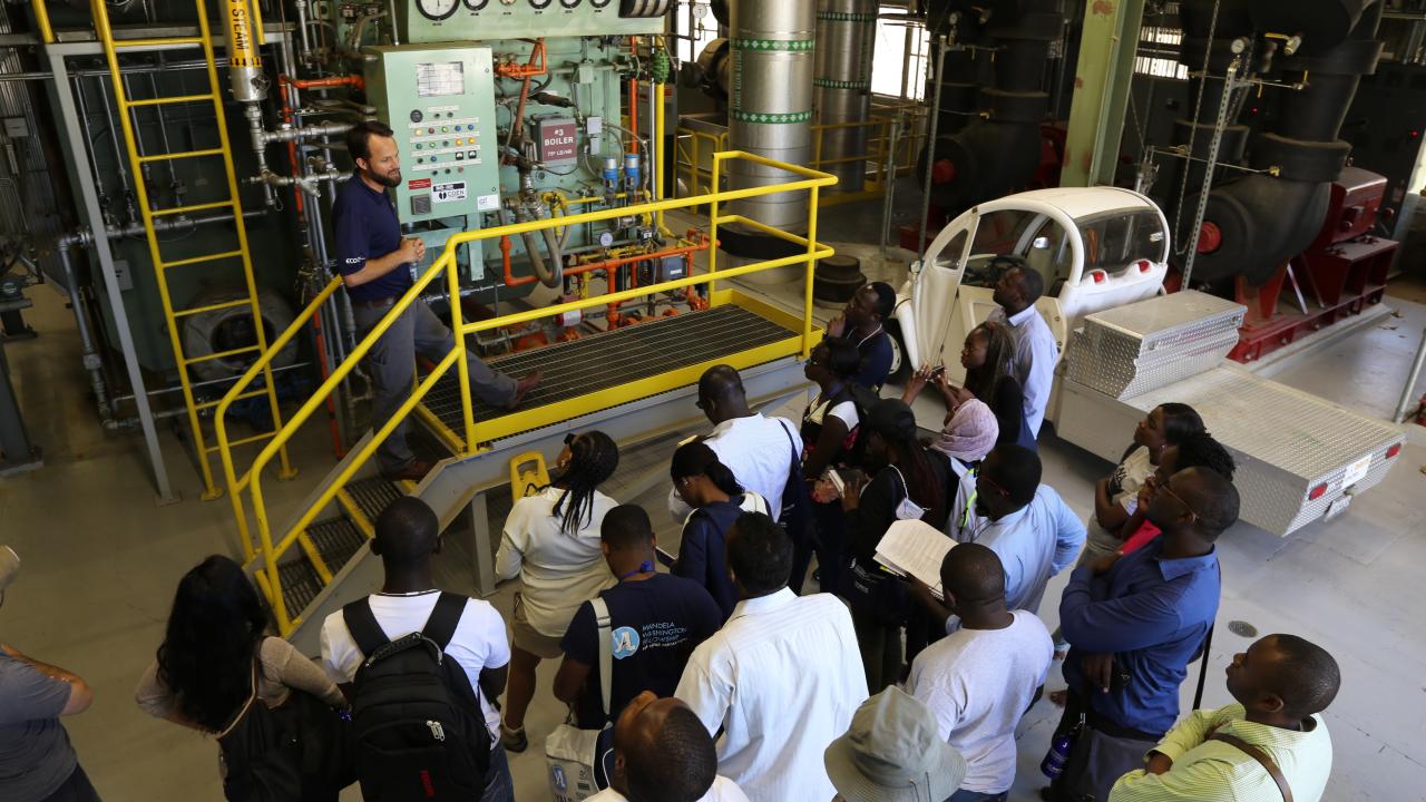 Joshua Morejohn stands in front of a steam system at UC Davis talking with group of visitors.