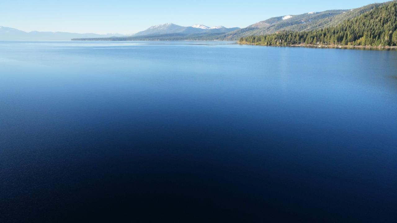Calm deep-blue Lake Tahoe with forested shore and distant mountains under clear sky