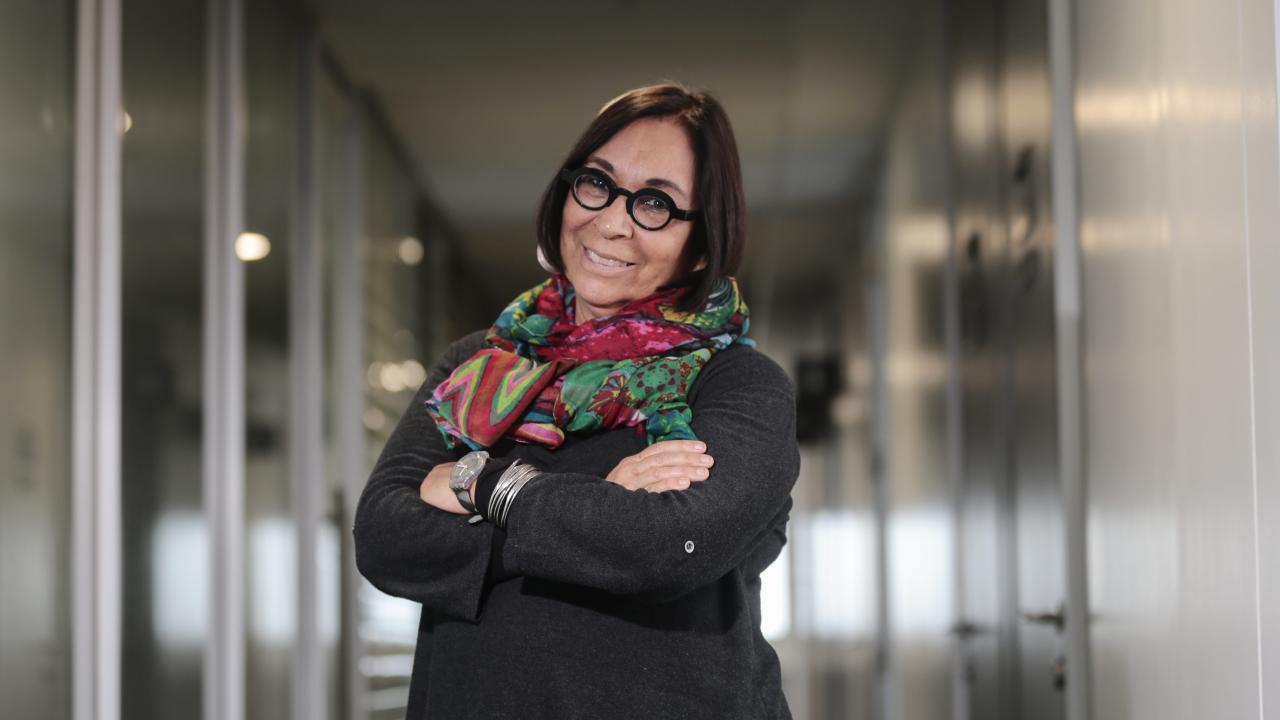 Smiling woman in glasses and colorful scarf, arms crossed in an office corridor