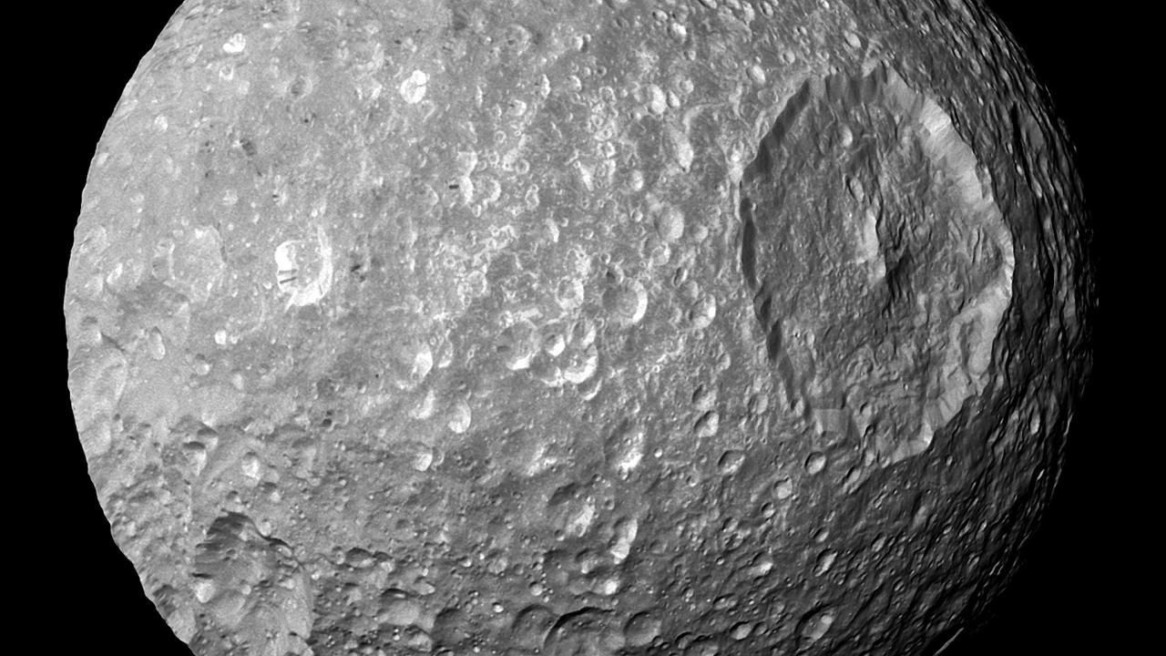 Grey ball pitted with craters with large crater on right hand side. Background is black. 