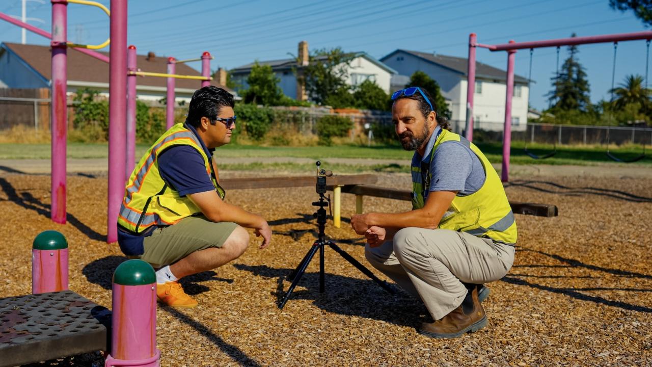 Two men in yellow construction vests squat on a schoolyard playground