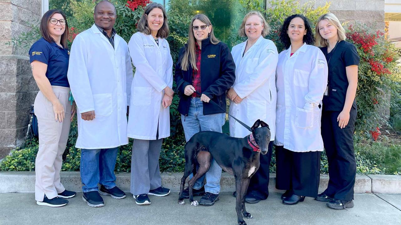 Group of people, many in labcoats, pose for photo with dog