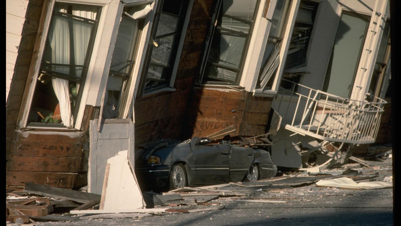 A car crushed by a sunken, tilting house. 