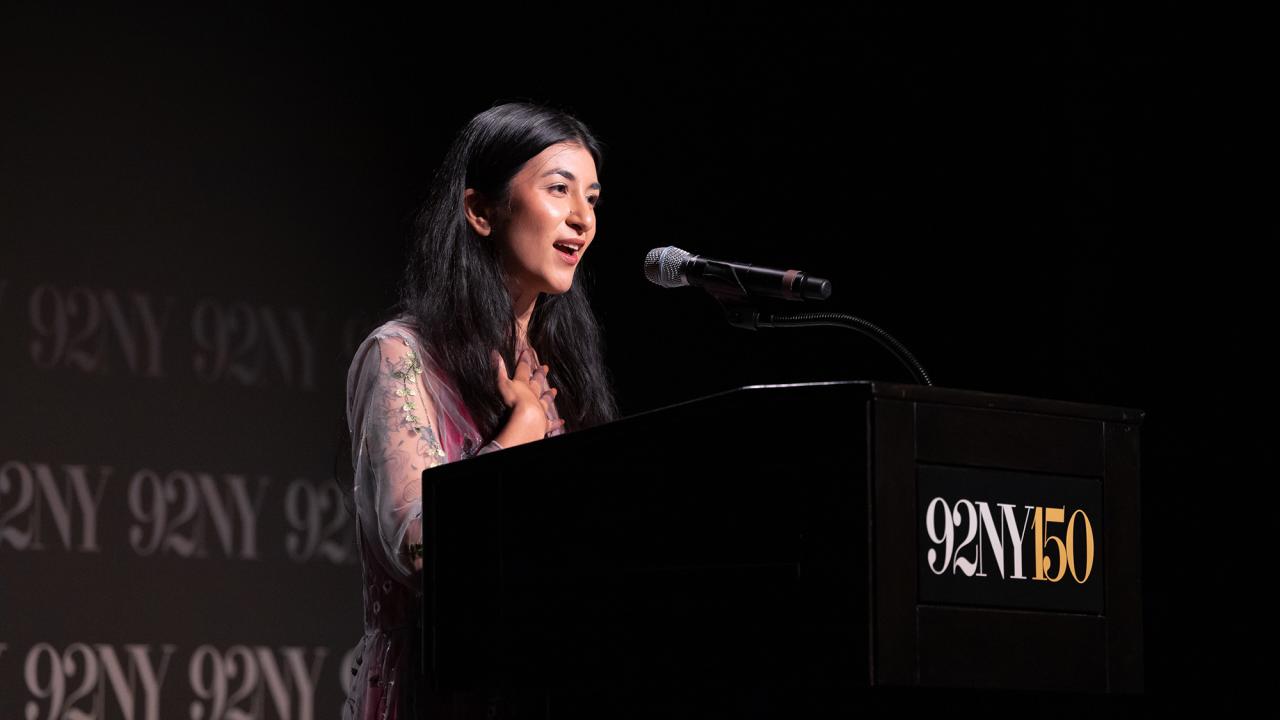 A young woman stands at a podium in a dark room