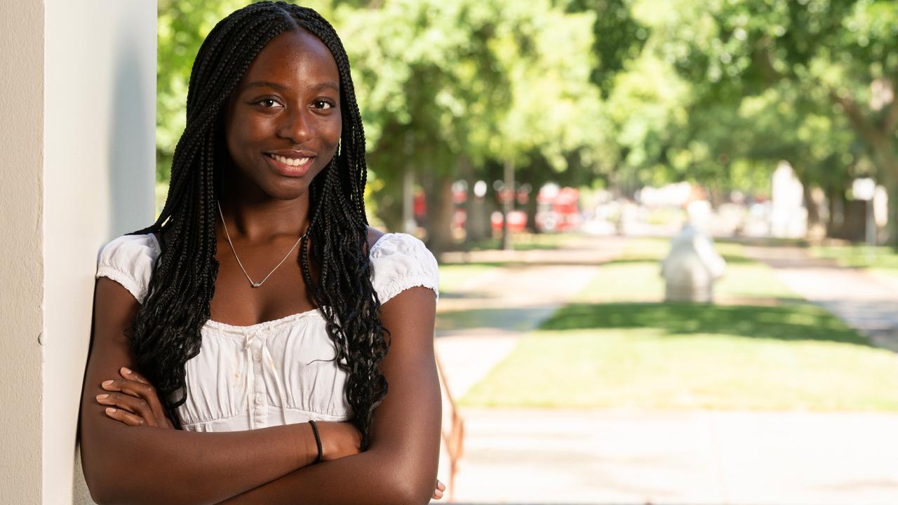 Student stands with her arms crossed with campus in the background