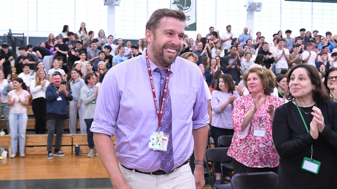 Smiling man in purple shirt walks past applauding crowd in gymnasium