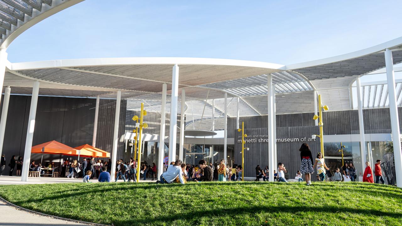 Crowds on lawn in front of white museum with see-through roof