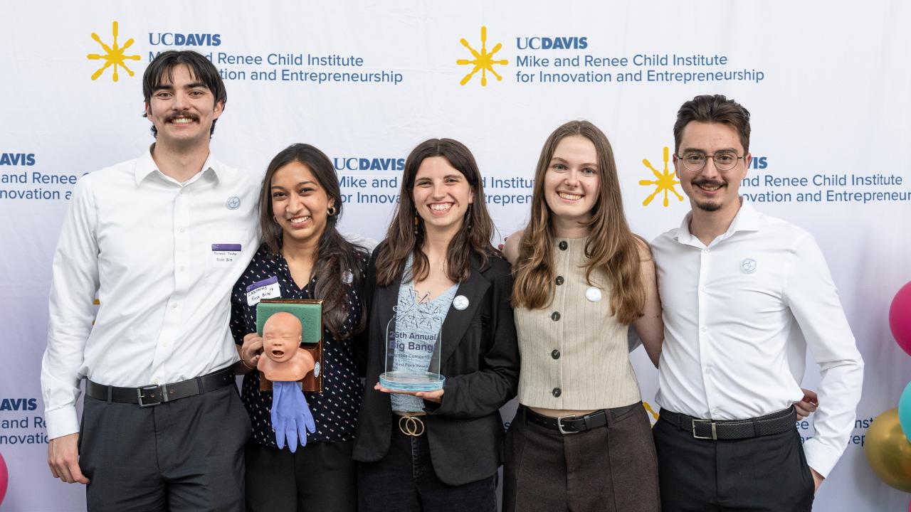 Six smiling people in business casual holding awards and a plush mascot against logo backdrop