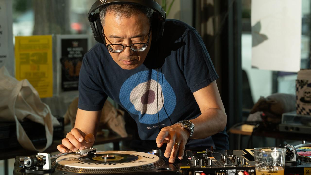 Man wearing headphones and blue target t-shirt adjusts vinyl on turntable in sunlit store