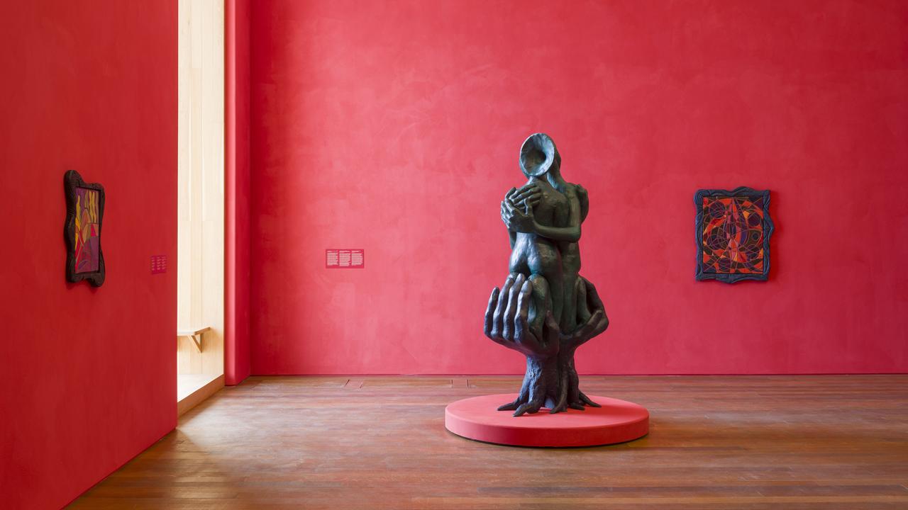 Museum gallery with red walls, wooden floor, and dark sculpture on round red plinth. Installation view: Woody De Othello: coming forth by day, Pérez Art Museum Miami, 2025–26. (Oriol Tarridas)