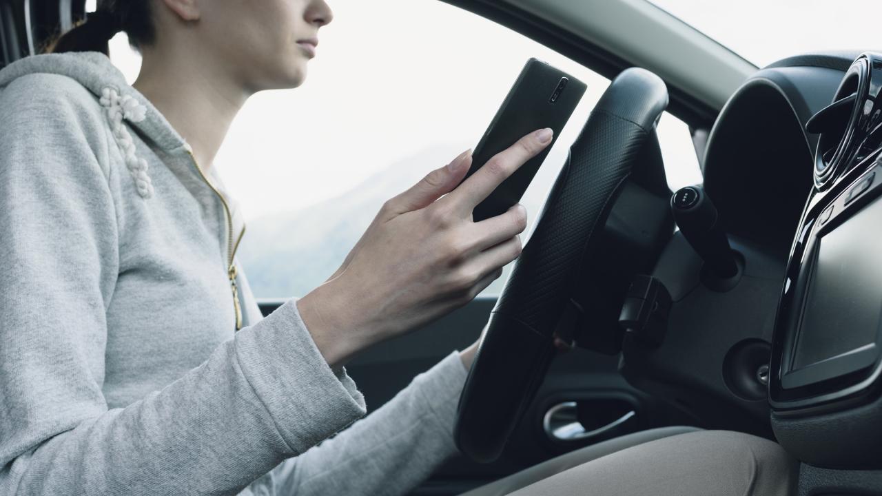 A young woman stops her car to look at her mobile phone.