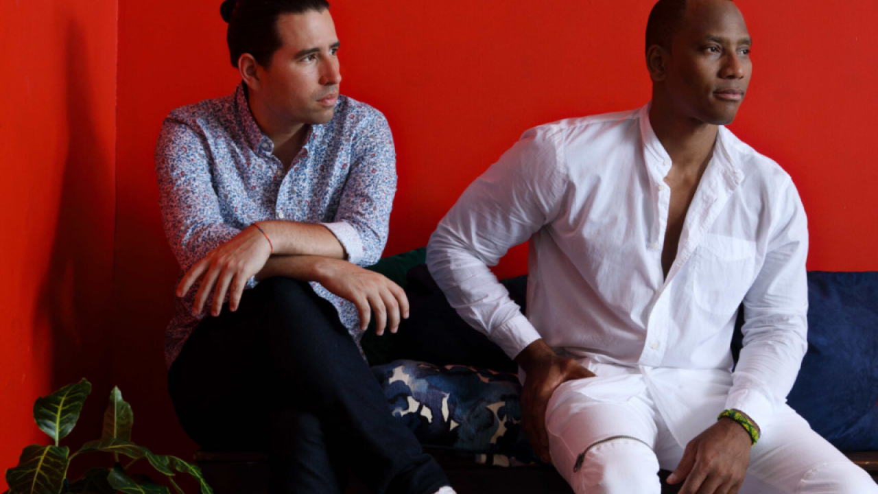 Two men sitting on couch with red background