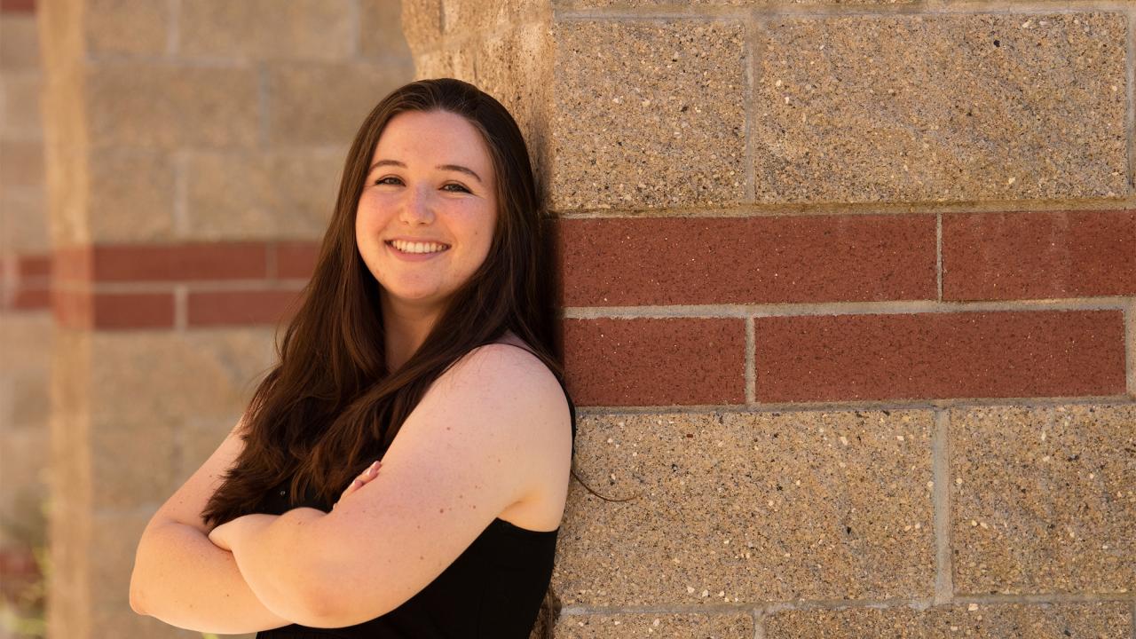 Amanda Portier leans against an exterior wall of the Alumni Center