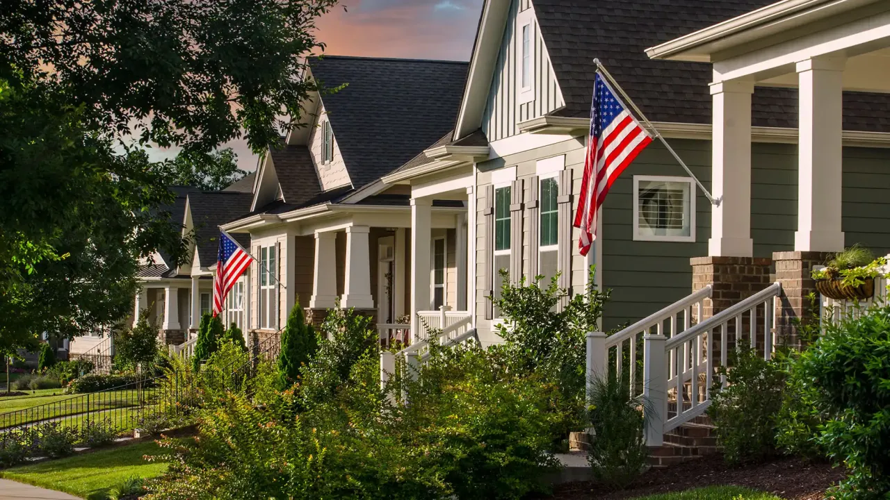 Suburban street scene with modest Craftsman style homes, American flags and green lawns.