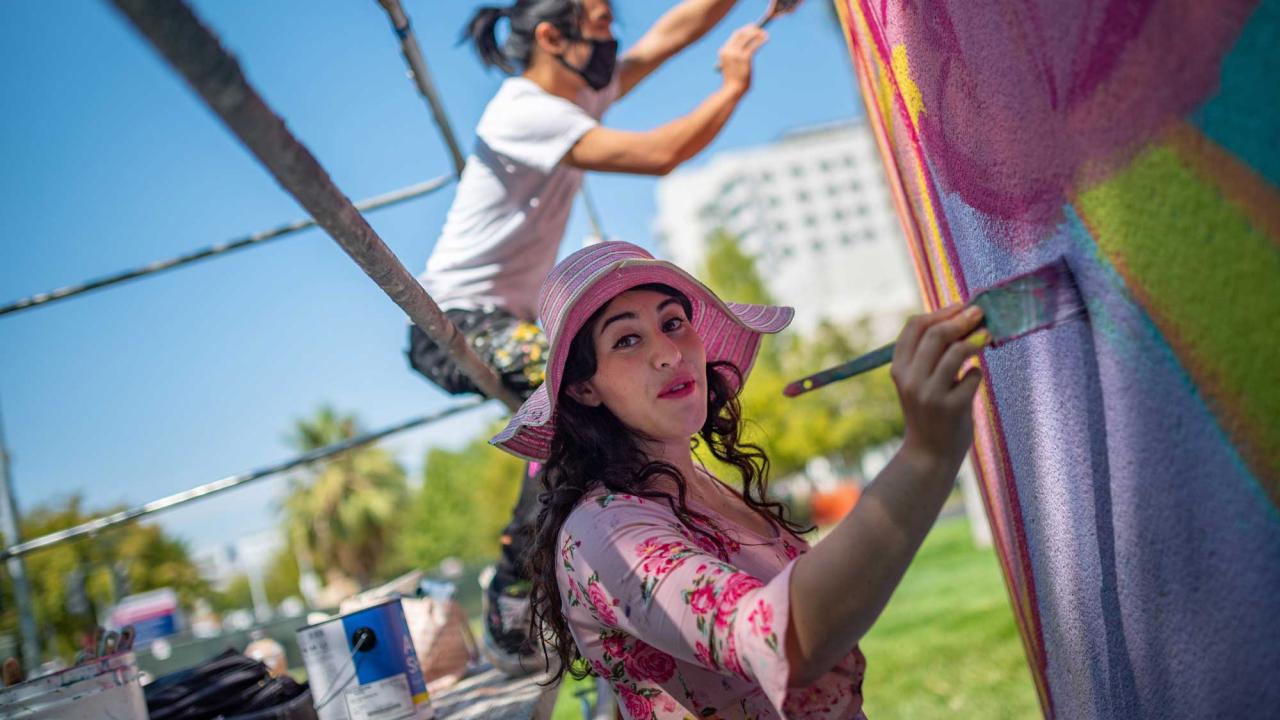 Woman closeup and man painting colorful mural on large wall.